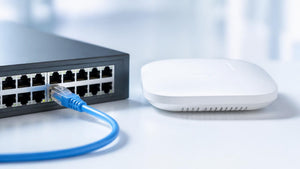 Blue Cat6 patch cable plugged into a PoE network switch beside a wireless access point | Conversions Tech
